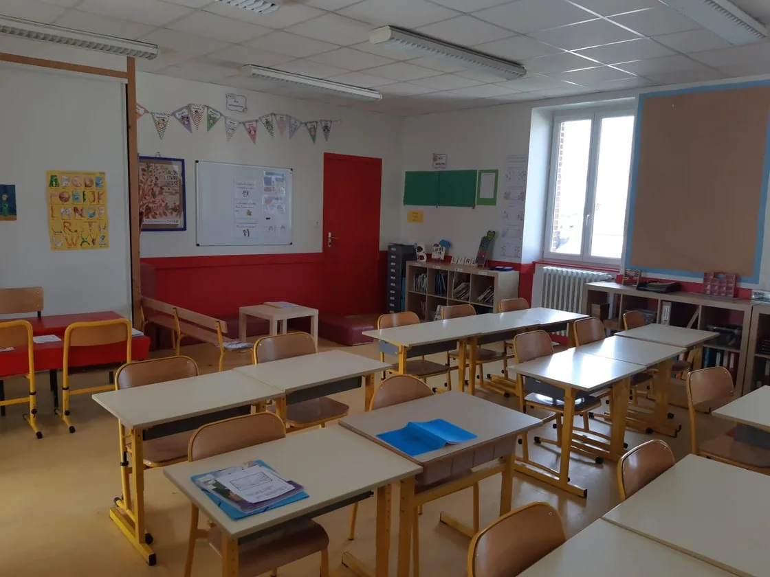 Une salle de classe aux tables alignées, dont un mur vient d’être repeint en rouge