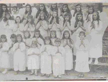 Photographie ancienne : un groupe de fillettes en robe blanche devant un mur de pierre