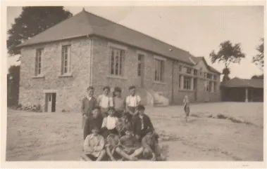 Photographie ancienne : des élèves rassemblés devant le bâtiment en pierre de l’école
