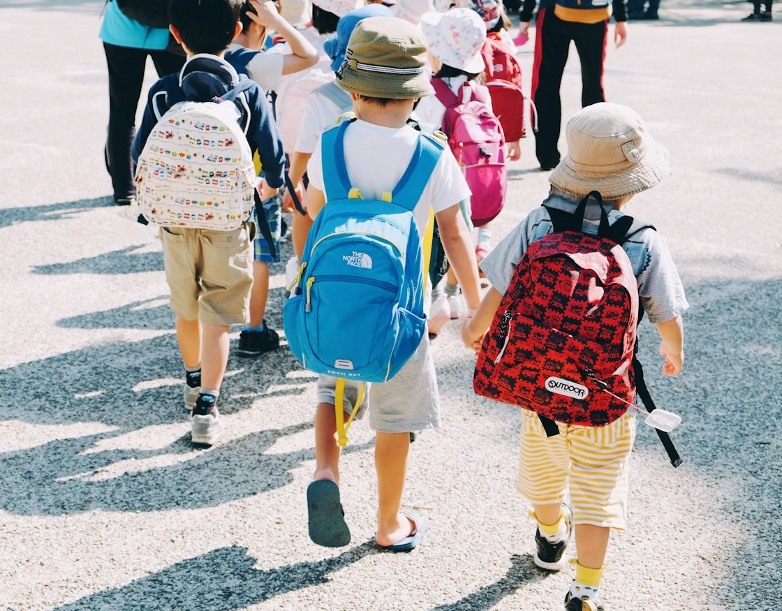 Un groupe d'enfants marche de dos lors d'une sortie, sacs à dos et chapeaux de soleil