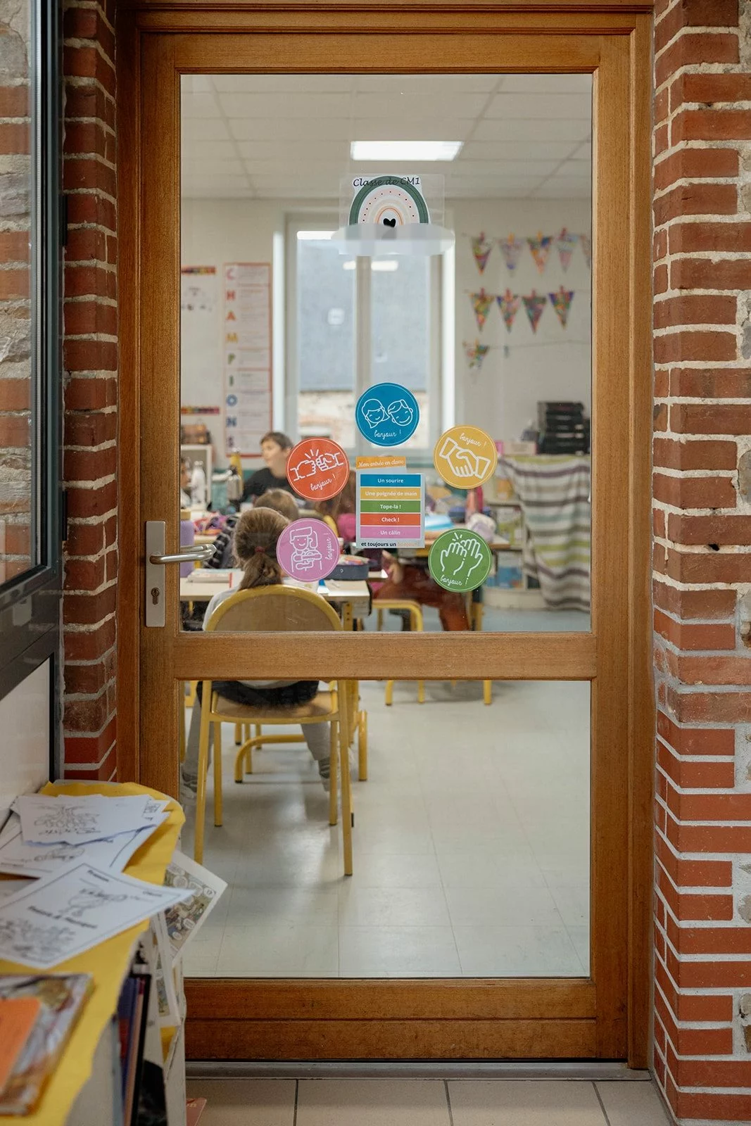 Une classe d’élémentaire vue à travers la porte vitrée, les élèves de dos à leurs tables