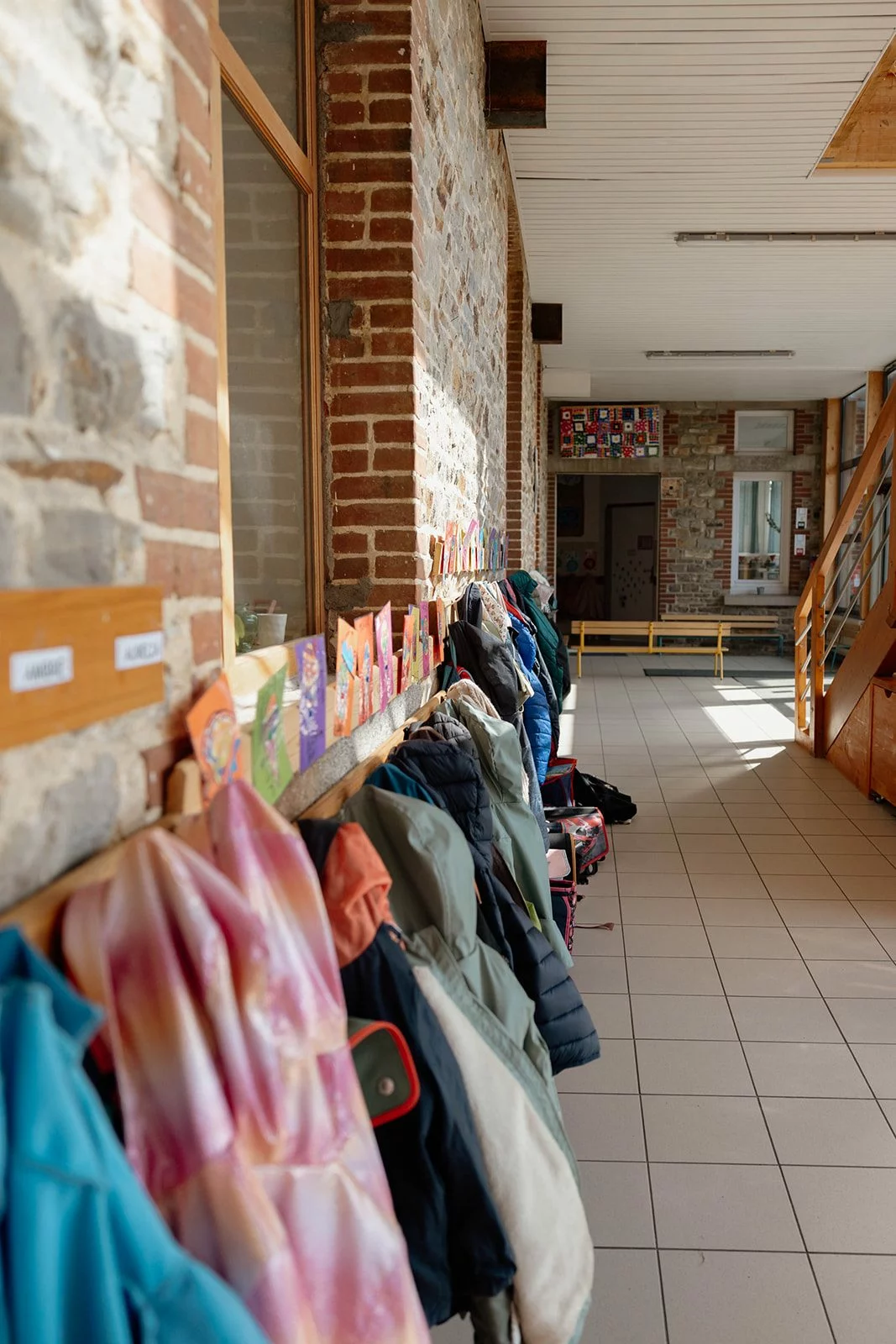 Le couloir de l'école et ses porte-manteaux, manteaux et sacs accrochés à hauteur d'enfant