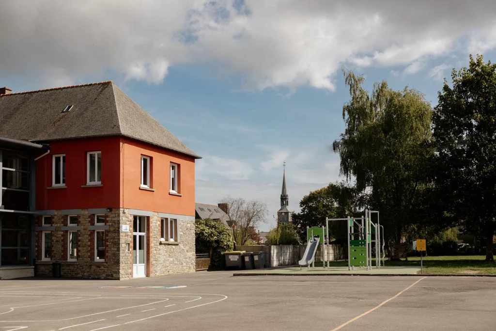 La cour de récréation de l'école et ses bâtiments, avec le préau vitré et l'aire de jeux