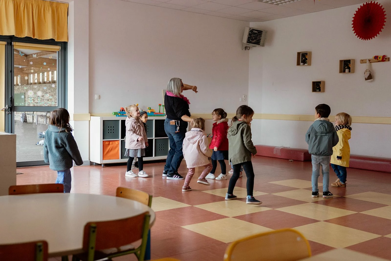Des enfants de maternelle imitent les gestes d’une adulte dans la salle de garderie