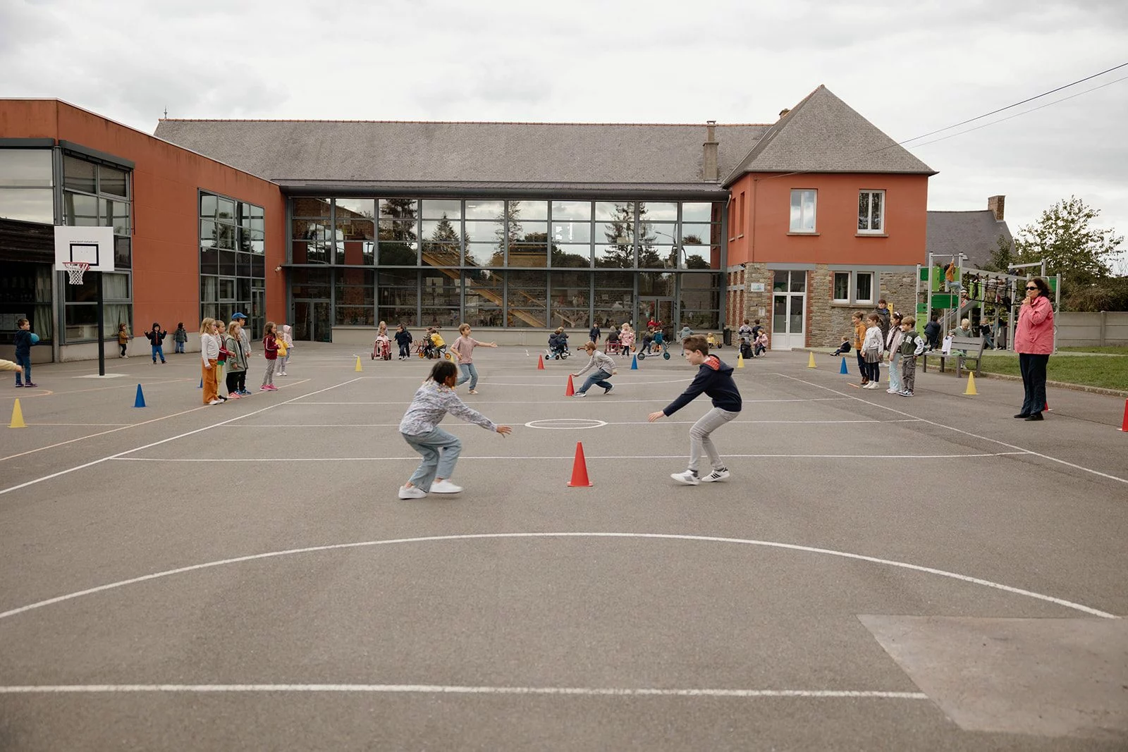 Deux élèves se font face au centre de la cour pendant un jeu collectif, le reste de la classe en cercle autour d'eux