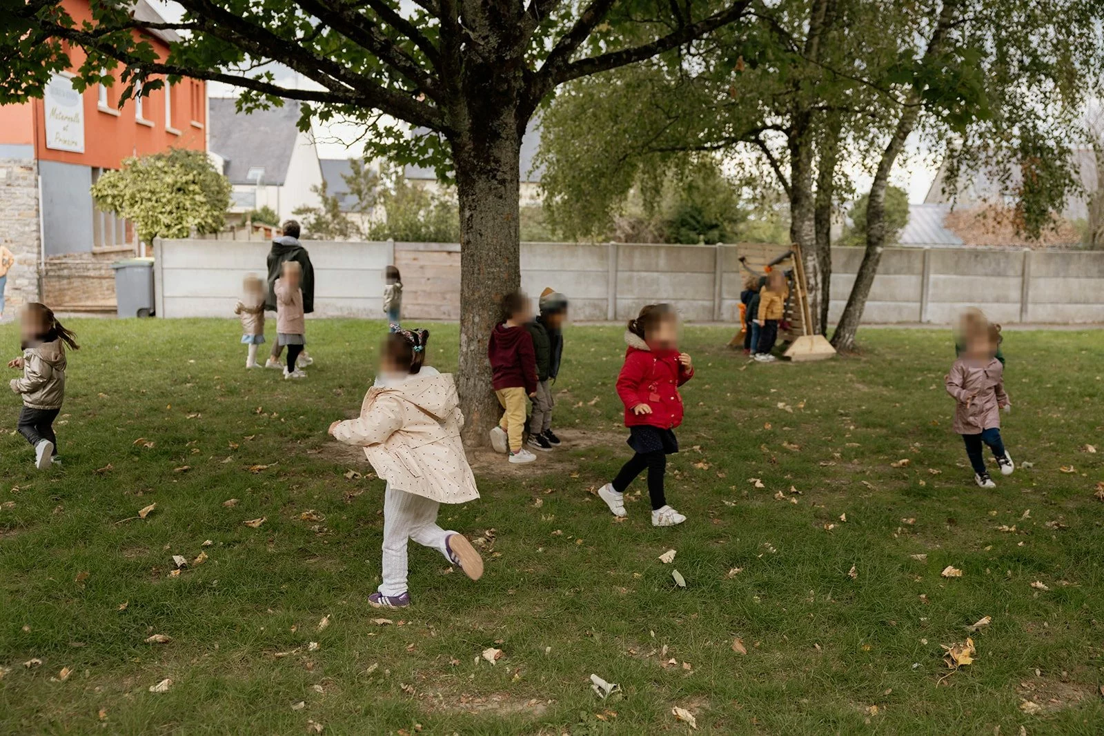 Des enfants de maternelle courent et jouent sur la pelouse ombragee de la cour