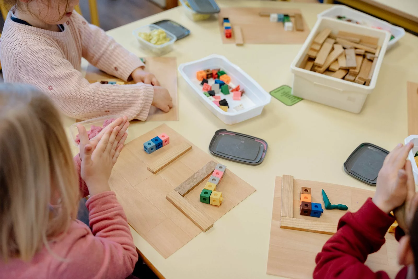 Des enfants de maternelle manipulent cubes, réglettes et pâte à modeler sur une table, vus de dessus