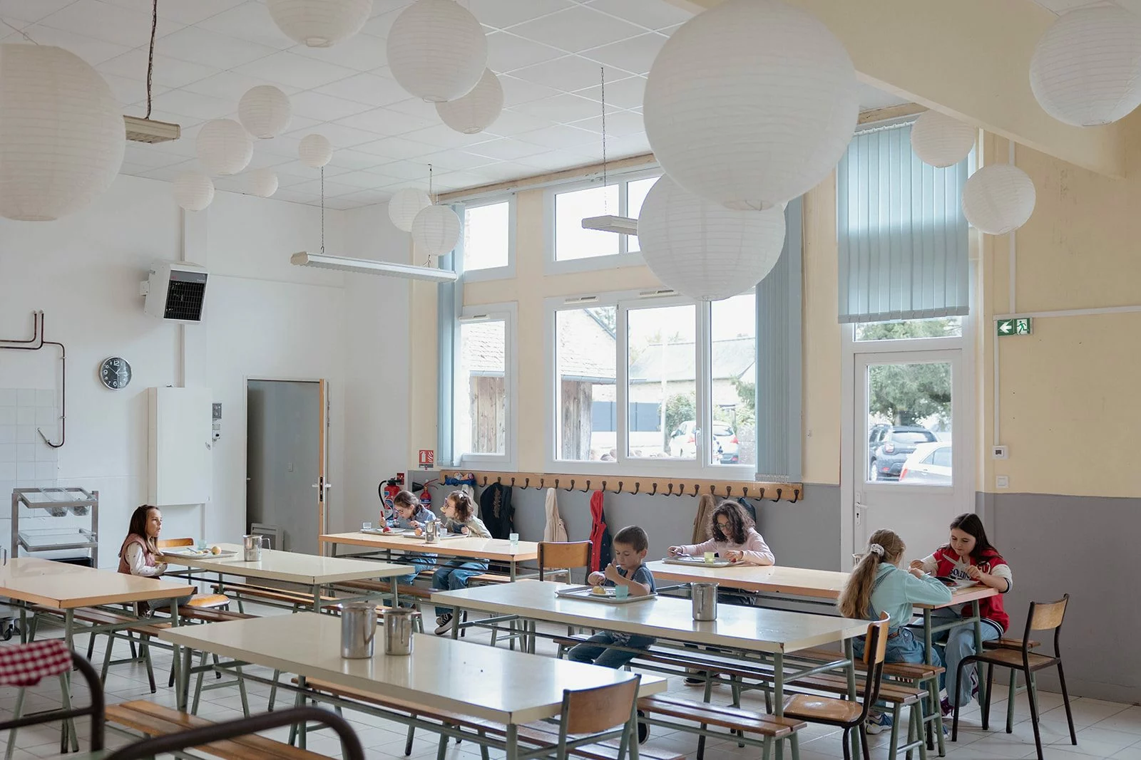 Des élèves déjeunent à la cantine sous les lampions de papier, les fenêtres ouvertes sur la cour