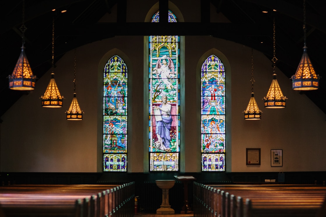 L interieur d une eglise : ses bancs de bois alignes vers le choeur et ses vitraux colores